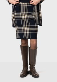 Granatowa spódnica w kratę z kremowymi akcentami, do kolan, uszyta z teksturowanej tkaniny. Połączona z brązowymi skórzanymi butami do kolan z czarną podeszwą.