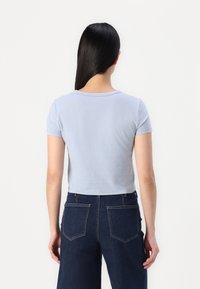 Camiseta corta de color azul claro con mangas cortas, cuello redondo y textura suave. Combinada con unos vaqueros de pierna ancha de mezclilla oscura que tienen bolsillos traseros.