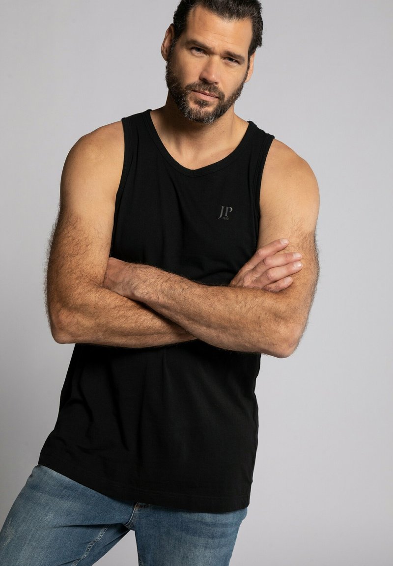 Schwarzes Baumwoll-Top mit Rundhalsausschnitt, das ein kleines "JP"-Logo auf der Brust trägt. Getragen mit blauen Jeans, die einen lässigen Look zeigen.