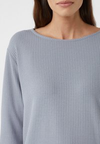Haut tricoté léger gris clair avec un motif texturé subtil, col large et manches longues, présentant une coupe décontractée et un tissu doux.