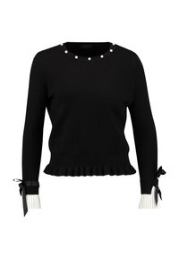 Pull en maille noire avec un ourlet festonné, des accents de perles autour du col, et des poignets plissés blancs ornés de rubans noirs.