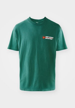 Camiseta de algodón verde con cuello redondo, mangas cortas y un gráfico en la parte frontal izquierda que presenta "OBEY DESIGN INDUSTRIES" y una explosión de estrellas roja.