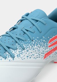 Close-up of blue sports shoe with blue laces, white speckled design, and red logo on the side.