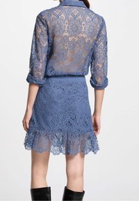 Robe en dentelle bleue avec motifs floraux, manches longues et ourlet évasé. Le tissu est transparent avec des détails texturés et une taille cintrée.