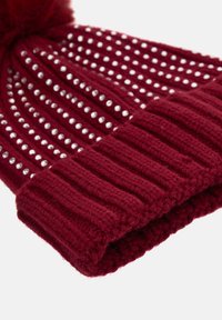 Cappello in maglia color bordeaux con una texture a coste, con borchie argentate disposte in linee verticali e un soffice pompon sulla parte superiore.