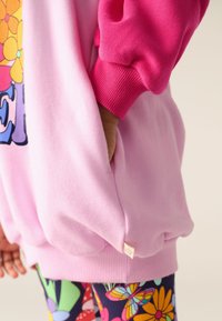 Rózsaszín pulóver színes virágmintával és ballon ujjakkal, bordázott mandzsettával és kis címkével a szegélyén.