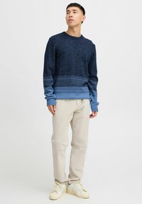 Marineblå og lyseblå teksturert genser med ribbede mansjetter, parret med kremfargede bukser og lyse sneakers. Enkel, avslappet design.