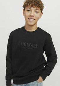 Svart sweatshirt i bomull, med rund halsringning och lång ärm. Framsidan har en texturerad "ORIGINALS"-logotyp.