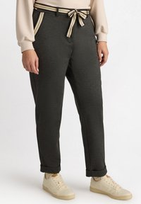Donkergrauwe broek met een bijpassende gestructureerde riem, met gestreepte accenten op de zakken. Gecombineerd met lichtgekleurde sneakers.