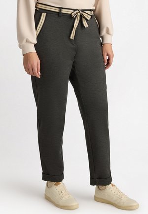 Donkergrauwe broek met een bijpassende gestructureerde riem, met gestreepte accenten op de zakken. Gecombineerd met lichtgekleurde sneakers.