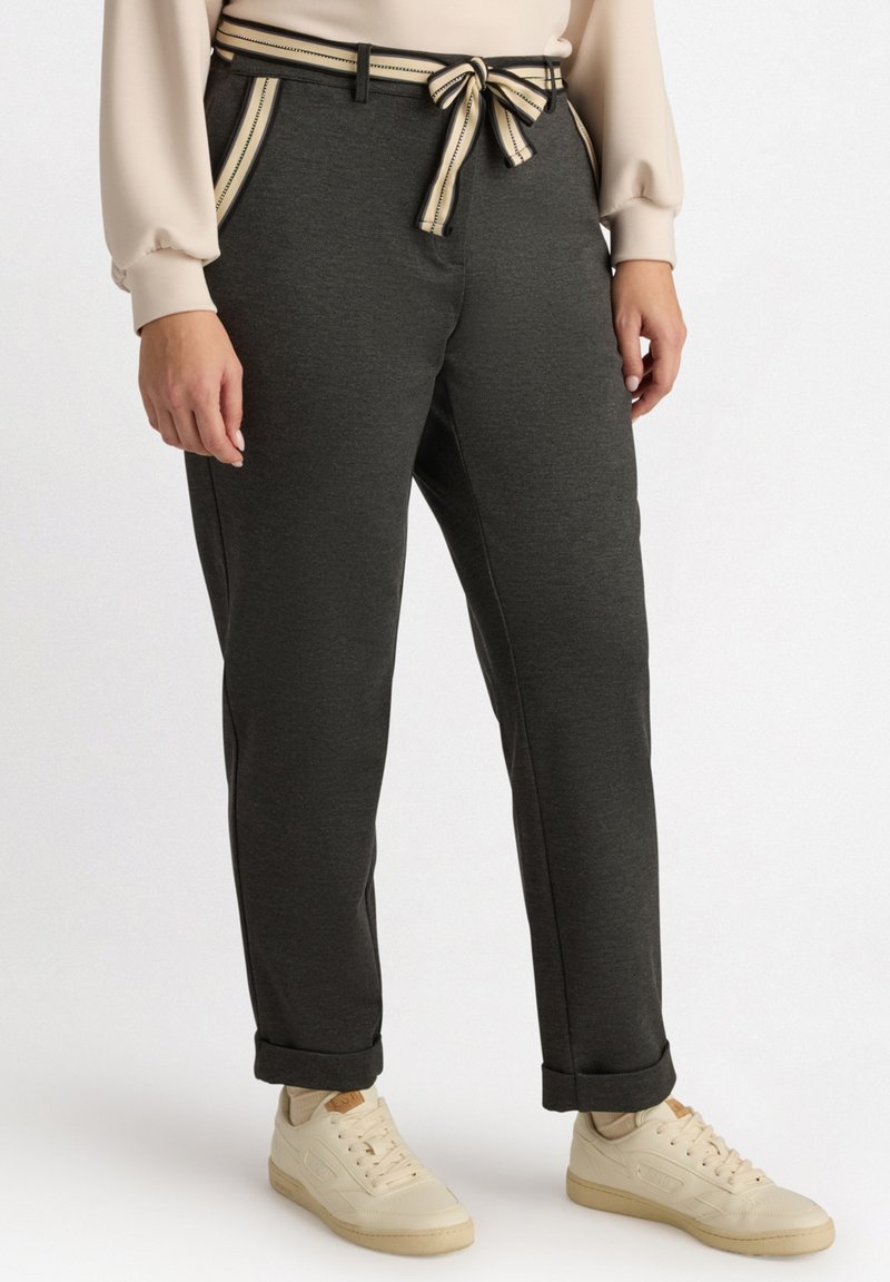 Donkergrauwe broek met een bijpassende gestructureerde riem, met gestreepte accenten op de zakken. Gecombineerd met lichtgekleurde sneakers.