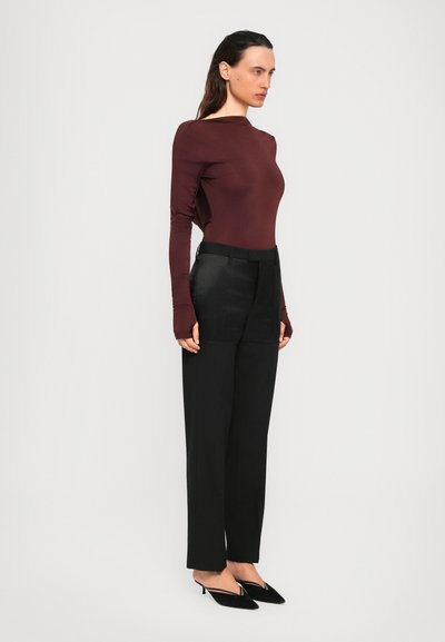 Woman in a fitted long-sleeve burgundy top, high-waisted black trousers, and black pointed kitten heels standing sideways.