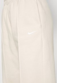 Light beige Nike sweatpants with a soft texture, featuring a white Nike logo on the left thigh and an elastic waistband.
