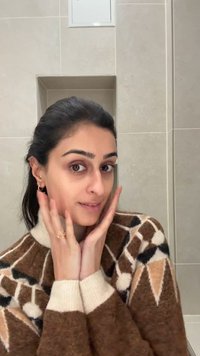 Brauner Strickpullover mit geometrischen Mustern und cremefarbenen Akzenten, Modell hält das Gesicht mit den Händen, neutraler Hintergrund, weiches Licht.