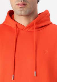 Orange hoodie made of soft fabric, featuring a front pocket, drawstrings with metal tips, and a subtle logo on the chest.