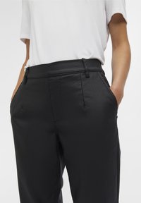 Zwarte broeken met een gladde textuur, voorzien van een aangesloten taille, twee zijzakken en een minimalistisch design. Gecombineerd met een witte top.