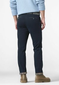 Marineblauwe chinos met een rechte snit, voorzien van achterzakken en een geprinte boord. Draagt een paar tan enkelboots en een lichtblauwe trui.
