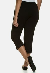 Zwarte cropped broek met een elastische tailleband, met zijsplitten aan de onderkant. De stof lijkt licht en glad te zijn.
