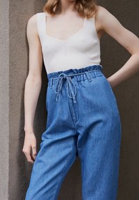 Body bianco a coste con scollo a V e pantaloni in denim blu a vita alta con life regolabile e vestibilità rilassata.