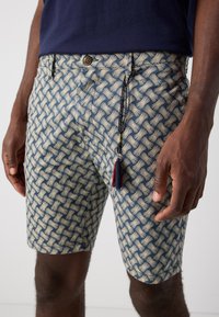 Patroongedekshorts met een geometrisch ontwerp in marineblauw en crèmekleur, met een trekkoorddetail en een kleine rode tassel aan de taille.
