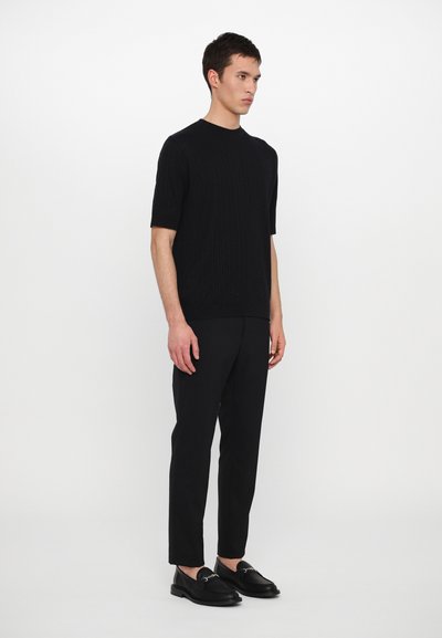 Top de punto negro de manga corta con textura acanalada, combinado con pantalones negros ajustados y mocasines negros. Textura suave y color uniforme en toda la prenda.