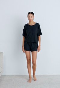 Svart kortärmad topp och matchande shorts i mjukt tyg. Toppens passform är avslappnad, medan shortsen har ett elastiskt midjeband.