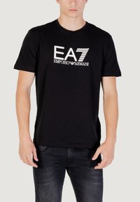 Camiseta de algodón negra con un logo blanco de "EA7 EMPORIO ARMANI" en el pecho. Mangas cortas y cuello redondo.