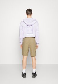 Lichtpaarse hoodie met een groot wit logo op de rug, gecombineerd met kaki shorts met een cargozak en logodetail.