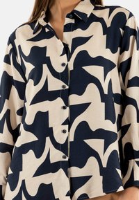 Camisa de botones hecha de una tela ligera, con un patrón abstracto en azul marino y crema, con cuello y cierre frontal de botones.