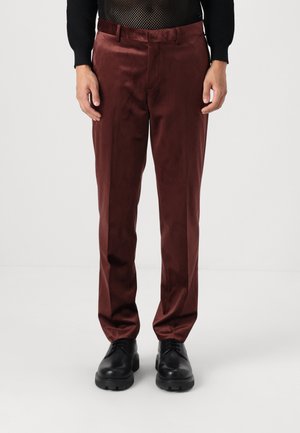 Burgundy trousers in a smooth, shiny fabric with a tailored fit, featuring belt loops and side pockets, paired with black lace-up shoes.