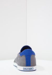 Sneaker in tela grigia con tacco e collare in tessuto blu, suola in gomma bianca e branding "HILFIGER" sul tacco.