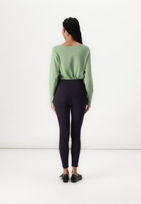 Grön långärmad tröja med avslappnad passform, kombinerad med högmidjade, mörkblå leggings. Outfiten avslutas med svarta låga klackskor.