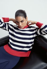 Maglione a righe in maglia con righe orizzontali blu navy e bianche, collo a coste rosso, orlo rosso in contrasto con bottoni decorativi.