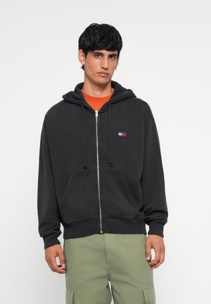 Schwarze Zip-Hoodie aus Baumwolle, mit einer Fronttasche und Kapuze mit Kordelzug. Mit einem kleinen, mehrfarbigen Logo auf der Brust akzentuiert.