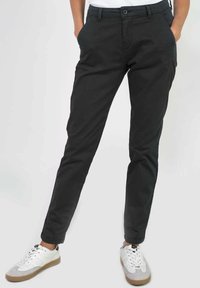 Zwarte chinos met een slim fit, gemaakt van katoen. Voorzien van zijzakken, een sluiting met een knoop aan de voorkant, en gecombineerd met witte sportschoenen.