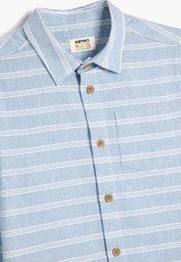 Camicia in cotone azzurro chiaro con righe orizzontali bianche, colletto button-down, bottoni in legno e taschino sul lato sinistro.