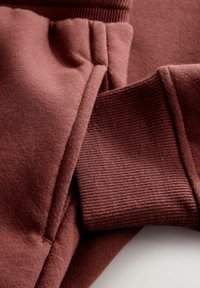 Bordo krāsa džemperis ar mīkstu, suflējošu tekstūru. Iezīmējas ar ribotām piedurknēm un gludu auduma izkārtojumu, izceļot šuvju detaļas.