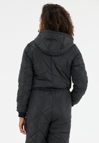 Zwarte gewatteerde jas met capuchon, met een diamanten patroon, elastische tailleband en ribgebreide manchetten. Gestructureerd synthetisch materiaal.