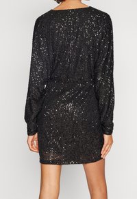 Robe noire à manches longues et coupe ample, ornée de sequins scintillants, avec un col rond et une taille élastique.