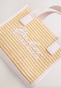 Kleine beige gewebte Handtasche mit hellrosa Lederhenkeln und besticktem „Nudie by Ted Baker“-Logo auf der Vorderseite.