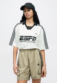 Fehér és fekete túlságosan nagy mez "ESPN" felirattal és fekete díszítésekkel, bézs rövidnadrággal, oldalcsíkkal és Adidas logóval. Fekete sapka.