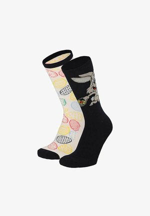 One black sock with a cartoon rabbit holding an Easter egg, and one white sock with colorful patterned Easter eggs.