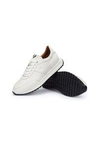 Zapatillas blancas de cuero con suela de goma negra texturizada, puntera redonda y cordones blancos. El interior es de cuero marrón con sutiles acentos del logo de la marca.