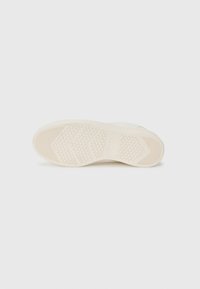 Cream-colored sneaker sole with textured rubber for grip, featuring hexagonal and linear patterns, smooth edges, and a minimalist design.