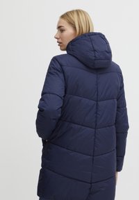Marineblauer Daunenjacke mit Kapuze, ausgestattet mit einem gesteppten geometrischen Muster, glatter Textur und langen Ärmeln, die bis zur Mitte des Oberschenkels reichen.