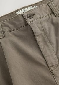Beige Baumwollhosen mit glatter Textur, ausgestattet mit einem Knopfverschluss und genähten Details entlang des Bundes und der Taschen.