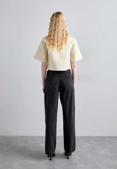 Cropped beige top with wide sleeves, paired with high-waisted black jeans. Smooth texture, minimal design, and no visible patterns or accents.