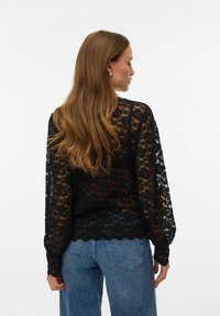 Blusa in pizzo nero con maniche lunghe, orlo smerlato e motivo floreale. Abbinata a jeans di denim a vita alta.
