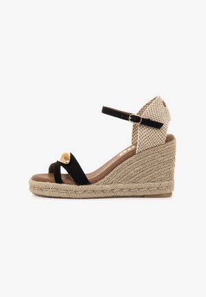 Sandalia cuña de ante negro con tacón tejido beige, con una sola tira y detalle dorado en la parte frontal. Correa ajustable en el tobillo.