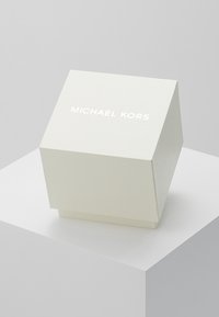 Weißer, strukturierter Geschenkkarton mit geometrischem Design, der auf der oberen Fläche das erhabene Logo "MICHAEL KORS" in Weiß trägt.